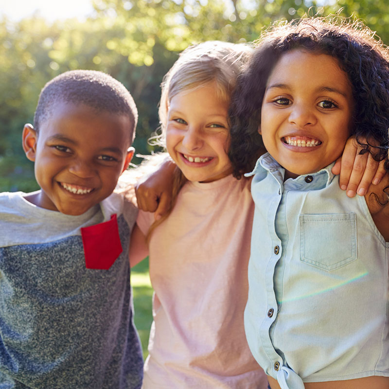 Three smiling young elementary age students with their arms around each other