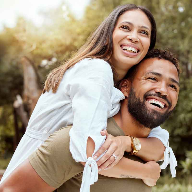 EFT and the Gottman Method, couple smiling with the woman on the man's back while outside in nature
