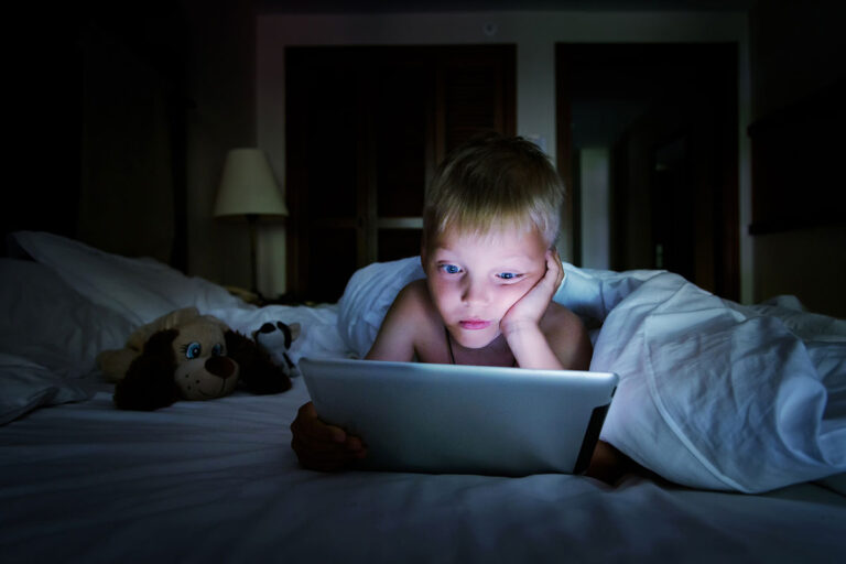 Talk to kids about current events, young boy looking at a tablet in the dark